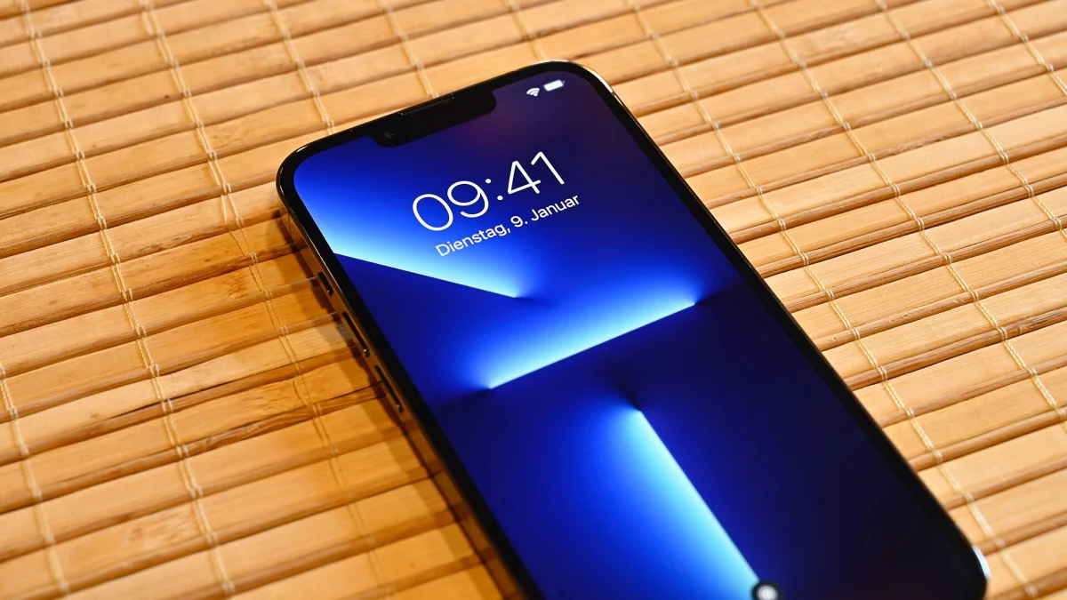 Un iPhone 13 Pro bleu posé sur une natte en bambou, écran allumé