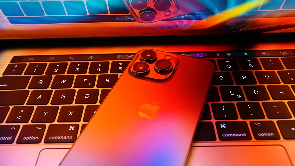 Un iPhone 13 Pro posé sur le clavier d’un MacBook Pro, sous un éclairage coloré